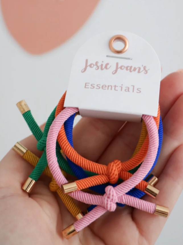 A set of 5 multicolored knotted hair ties with gold details, displayed on a card holder with 'Josie Joans Essentials' written on it.