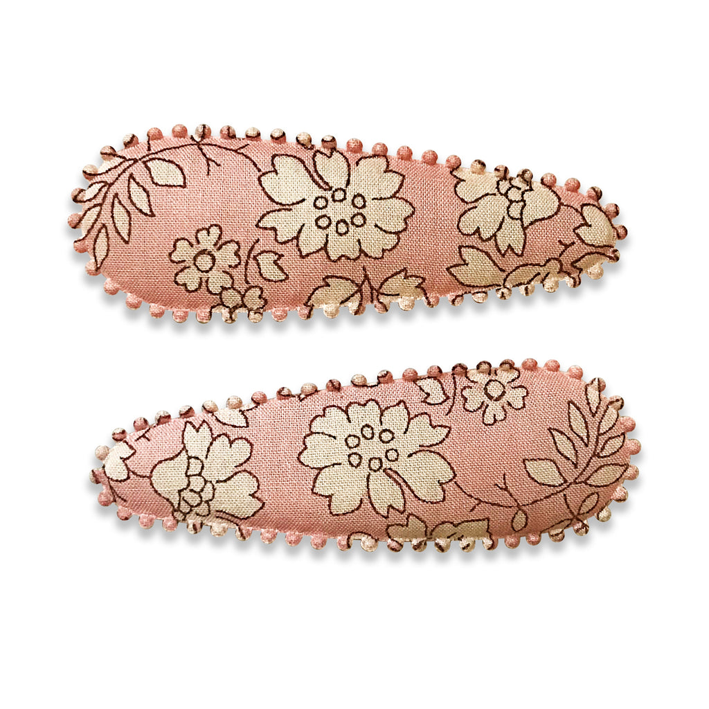 Two fabric-covered snap hair clips with a floral pattern and scalloped edge detail, in shades of pink and beige.