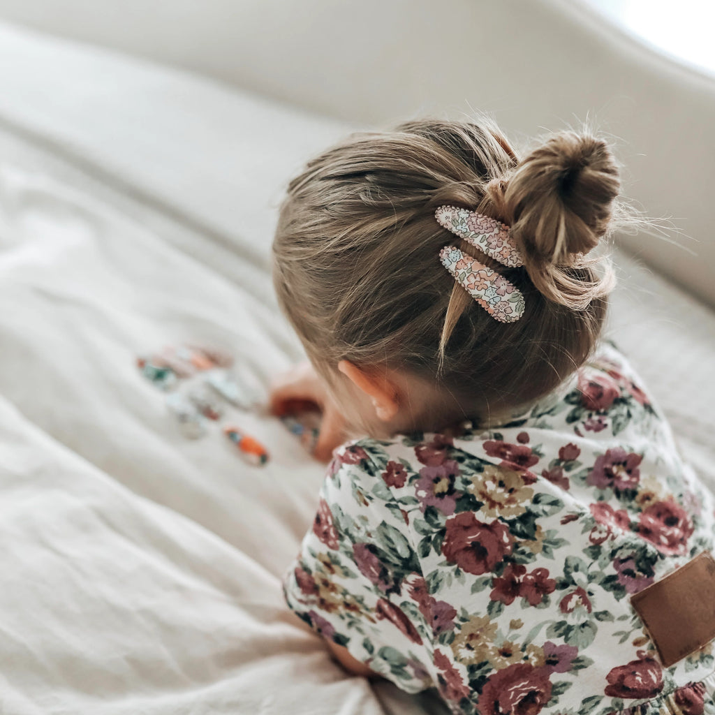 Child with a floral bib and hair tie on a white blanket