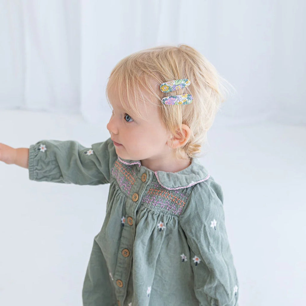 Child wearing a green dress with floral embellishments on a plain background