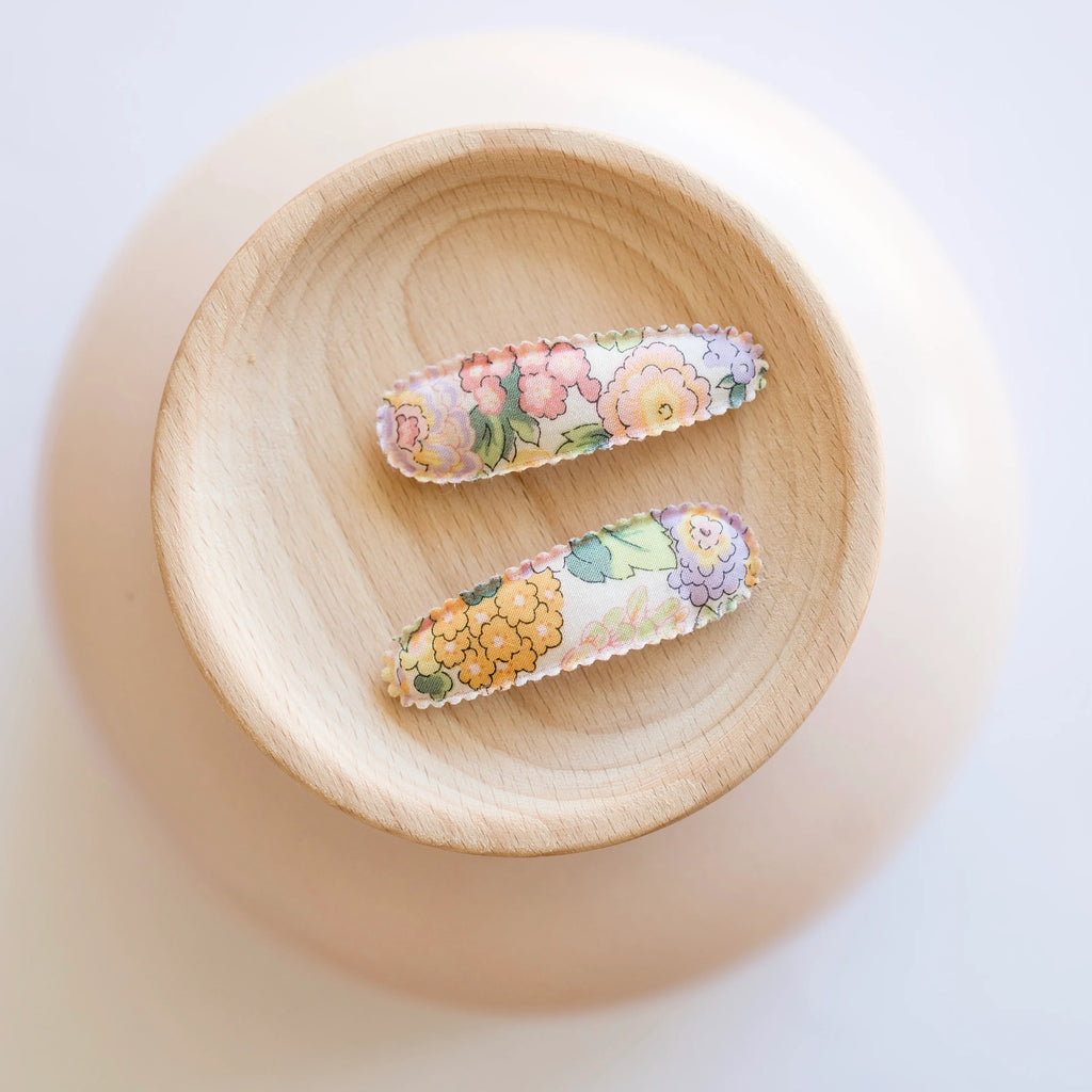 Two floral hair clips on a wooden plate with a soft focus background