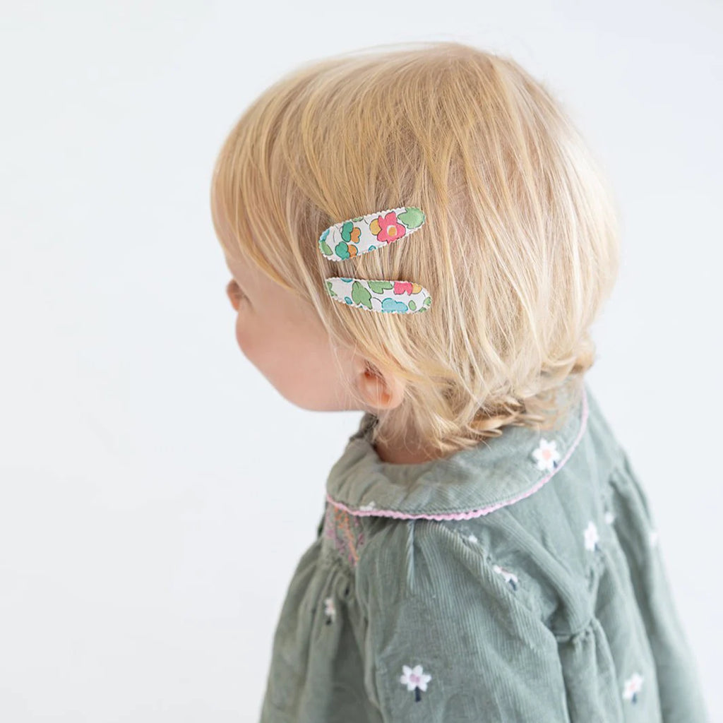 Child with floral hair clips on a plain background