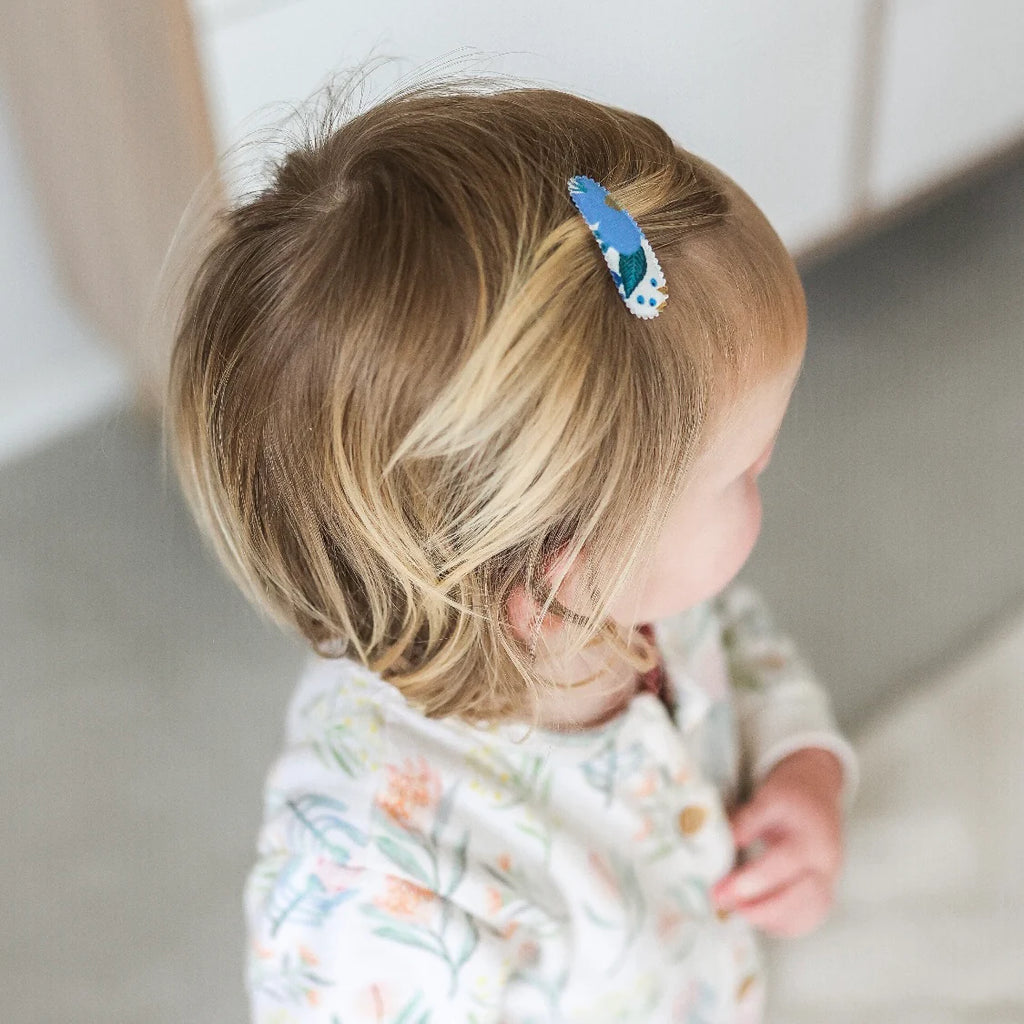 Child with a blue hair clip in their hair, wearing a patterned outfit.