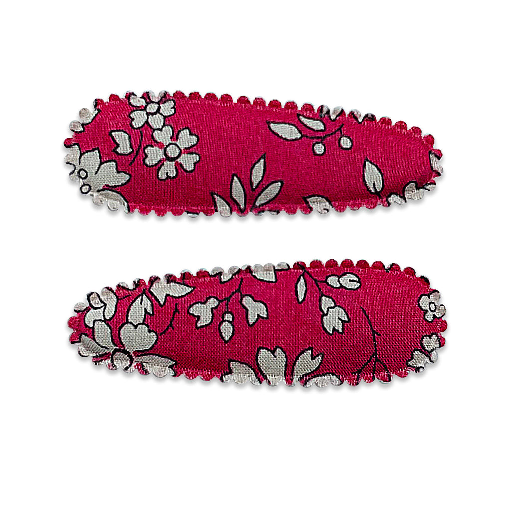 Set of two small fabric-covered snap hair clips featuring a deep pink background with an off-white floral Liberty-style print and scalloped stitched edging.