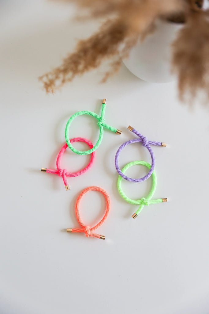Five Josie Joan's Neon Nora Hair Ties arranged on a white surface in neon green, purple, pink, and orange colours.