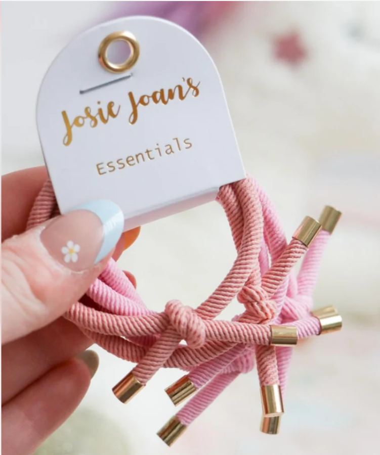 Hand holding a set of pink Josie Joan’s Essentials hair ties, featuring soft cord texture, knotted design, and gold metal tips on a white branded card.