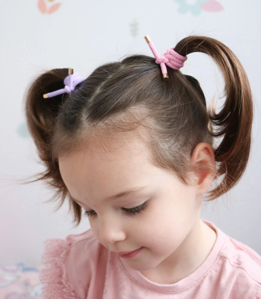 Child with pigtails wearing a pink shirt against a light background