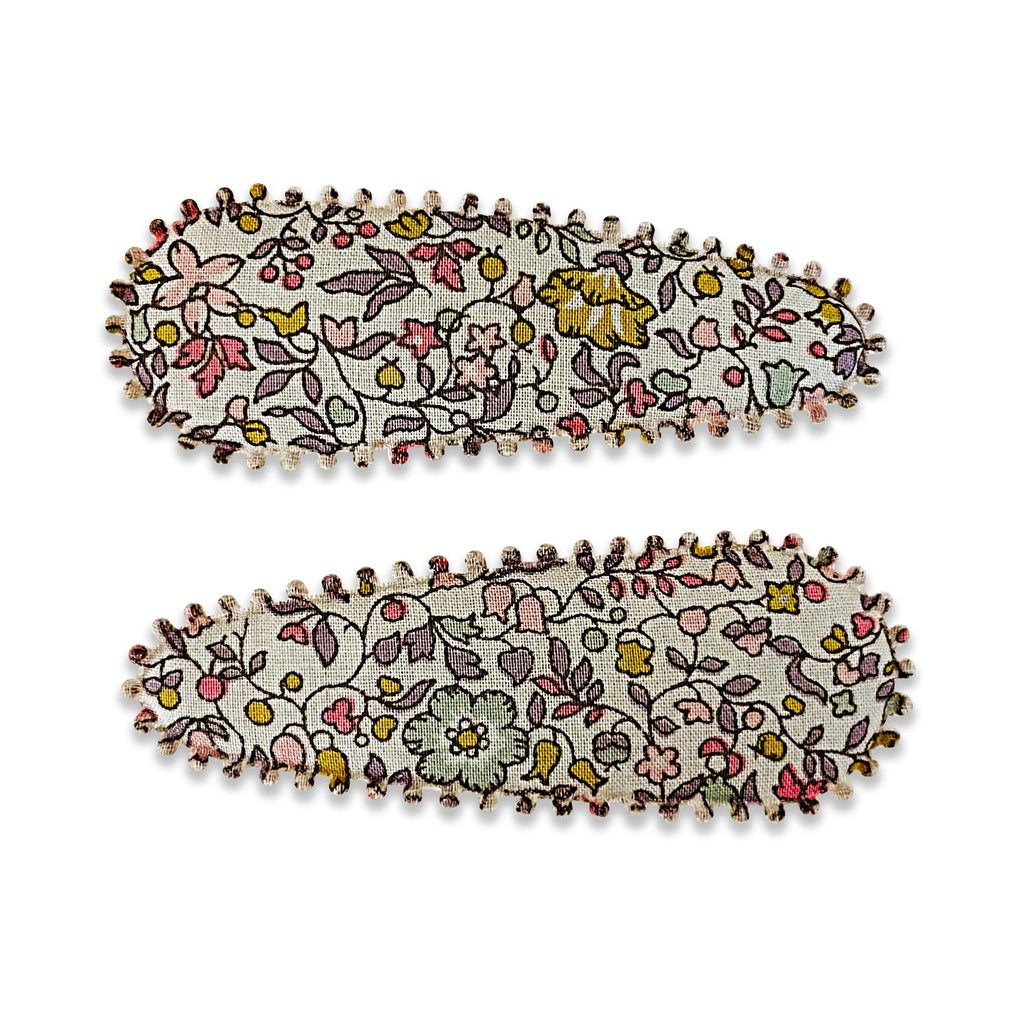 A pair of fabric-covered snap hair clips featuring a delicate floral print in soft pink, yellow, and green tones, finished with scalloped embroidered edges.