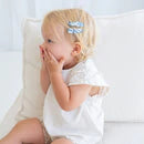 Child wearing a white outfit with a decorative hair clip on a light background