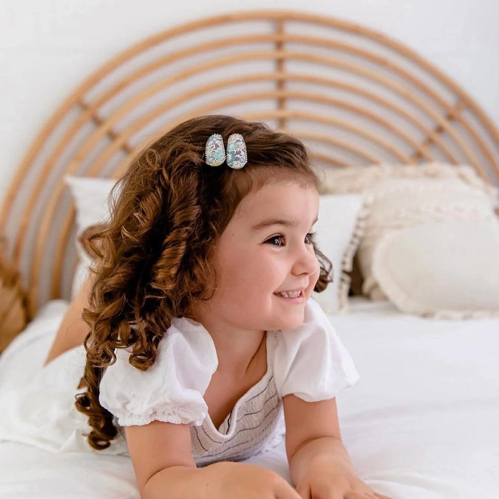 Young girl with curly hair and decorative hair clips sitting on a bed.