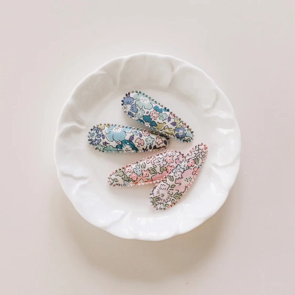 Two floral-patterned hair clips on a white plate with a light pink background