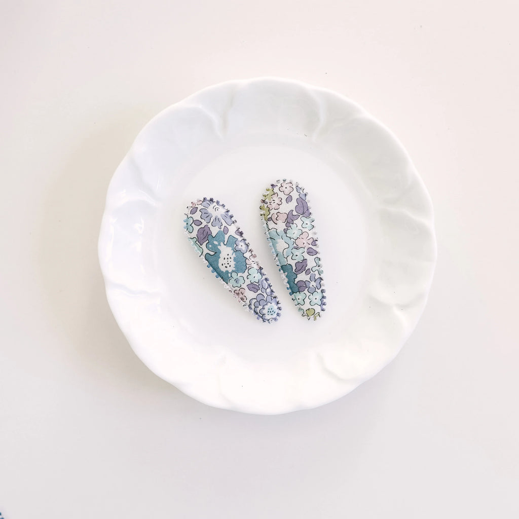 Two floral-patterned hair clips on a white plate with a white background