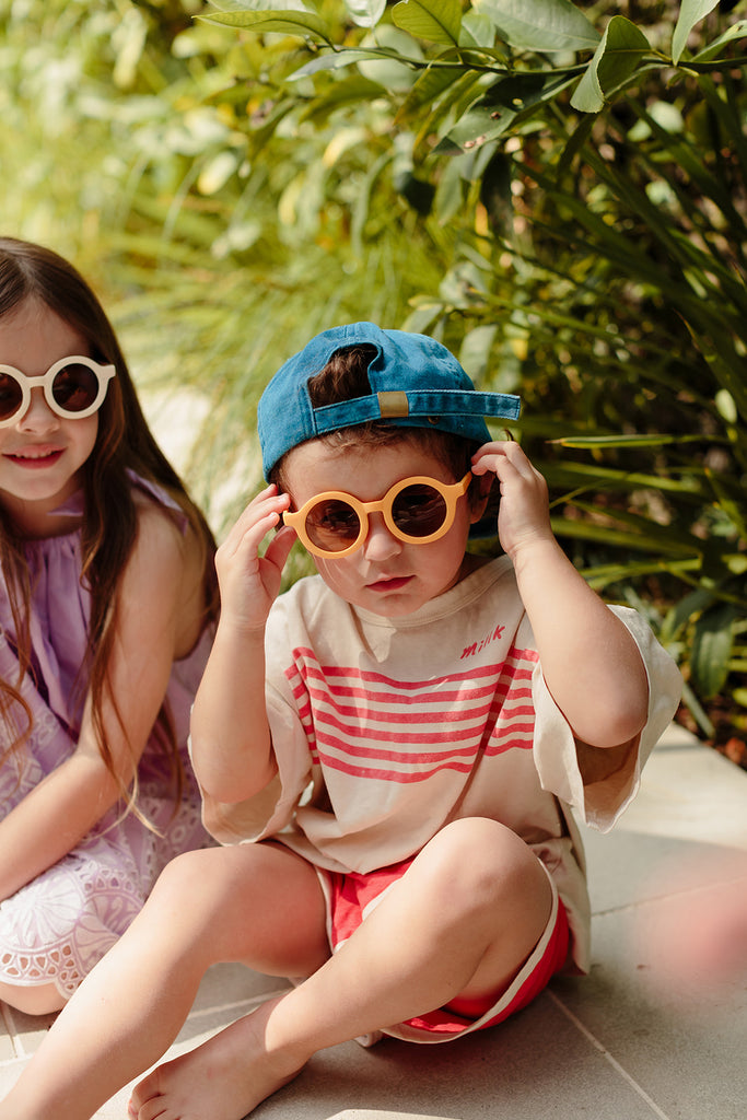 Sand-coloured kids’ sunglasses with a rounded frame displayed on a neutral light background.