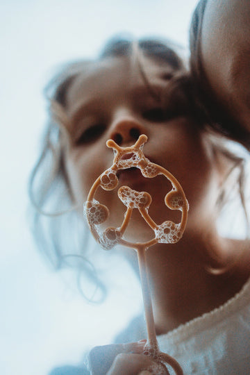 Close-up of girl blowing bubbles with eco-friendly lady bug wand in soft natural light.