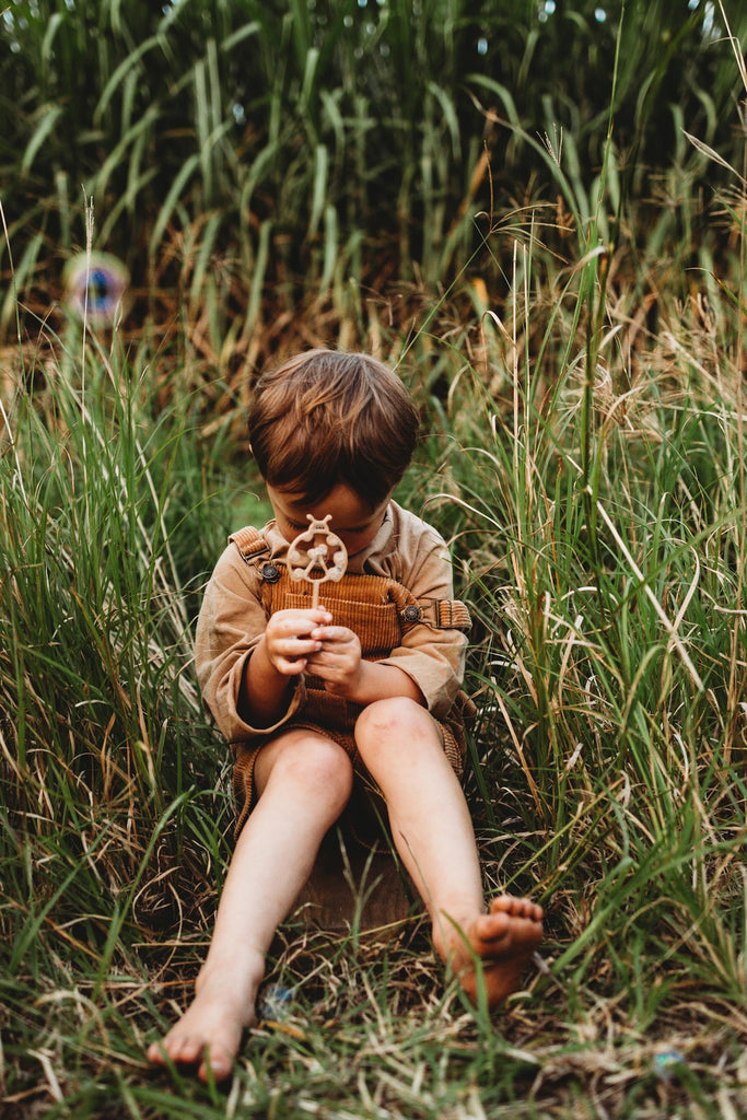 Child sitting in tall grass holding Kinfolk Pantry Lady Bug Eco Bubble Wand made from recycled sawdust and PLA bioplastic.