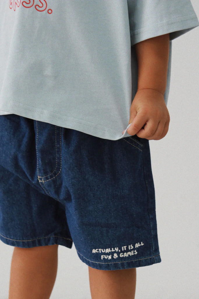 Close-up of a child wearing Lenn Label Fun & Games shorts, highlighting the 'Actually, it is all fun & games' embroidery detail.