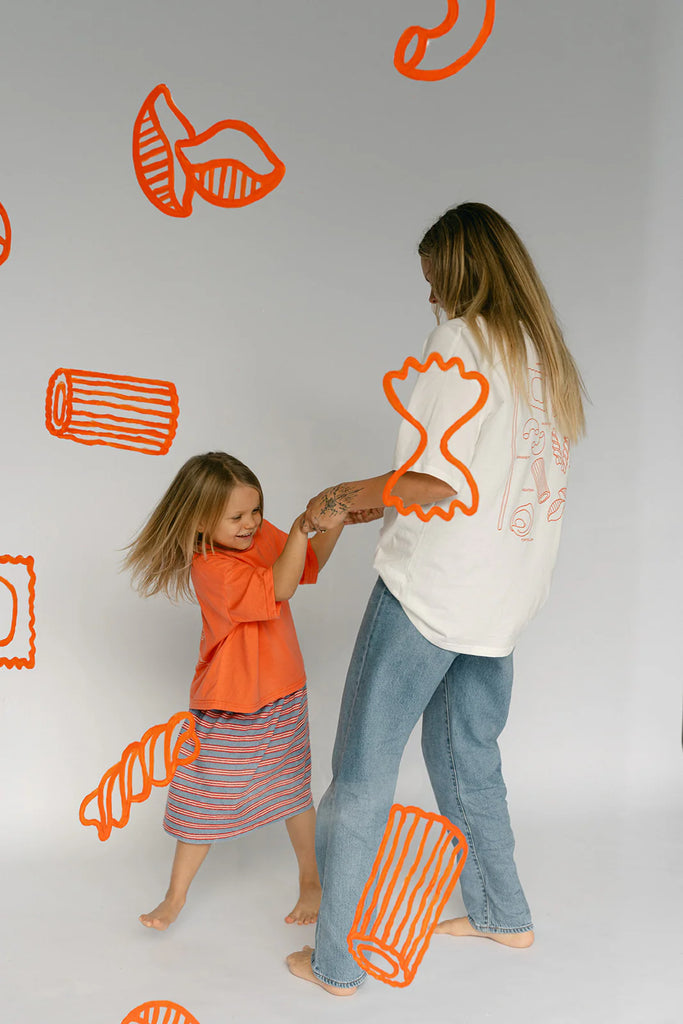Woman wearing Lenn Label Women's Pasta Tee dancing with a young child against a pasta-themed backdrop.