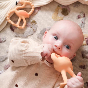 Baby lying on a patterned rug with a teething toy in mouth