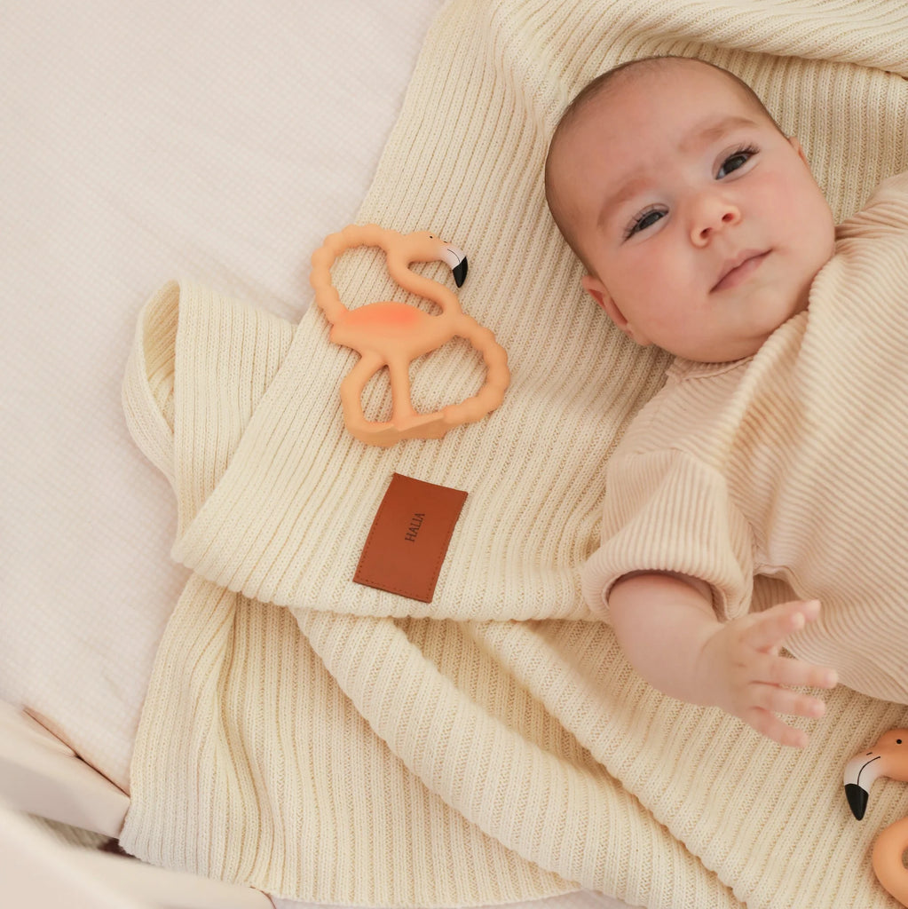 Baby wrapped in a beige blanket with a teething ring nearby