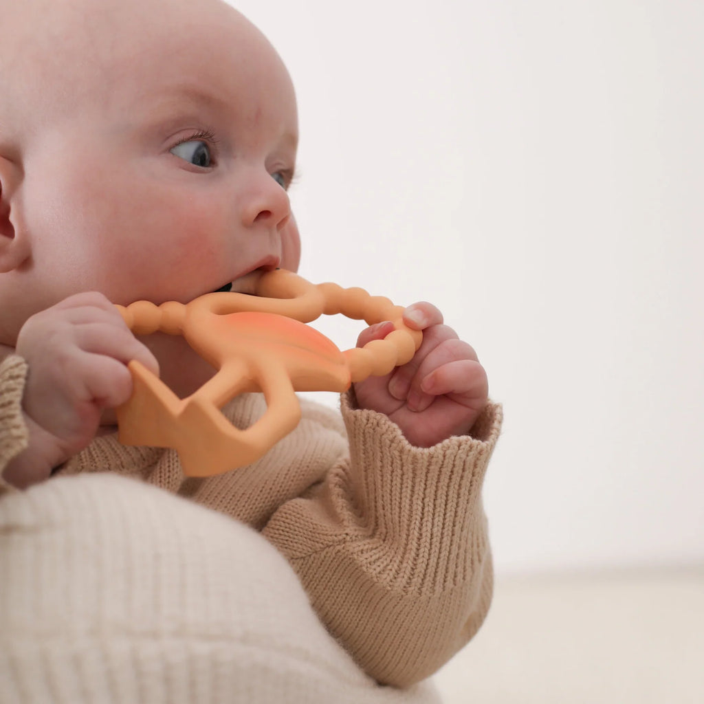 Baby holding an orange teething toy against a plain background