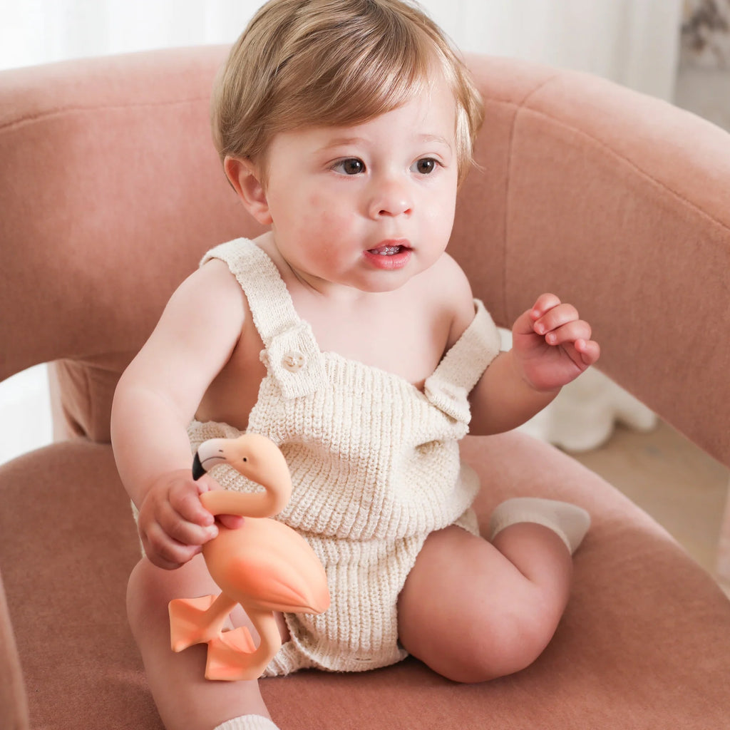 Baby in a beige romper holding a toy duck on a pink chair