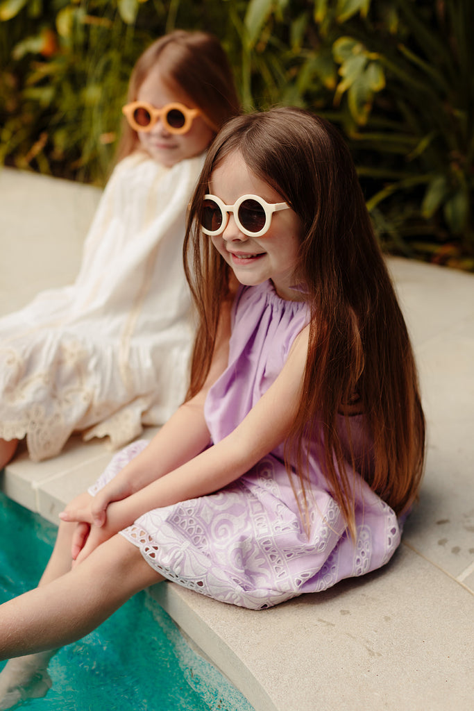 Bone-coloured kids’ sunglasses with rounded frames displayed on a soft cream background.