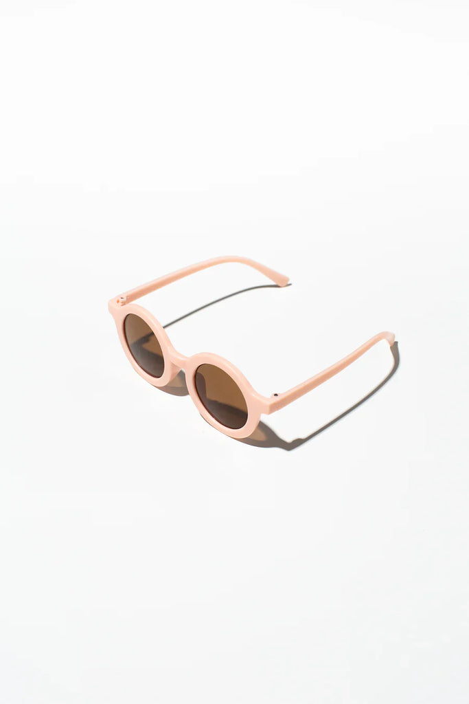 Peach-coloured kids’ sunglasses with a rounded frame displayed on a soft cream background.