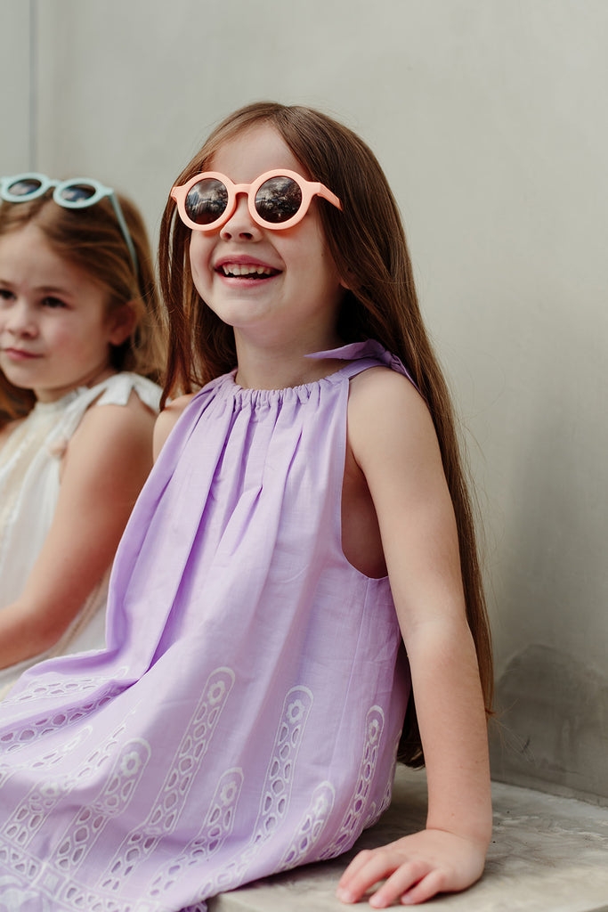 Peach-colored kids’ sunglasses with round frames displayed against a soft neutral background, showing their simple, modern design