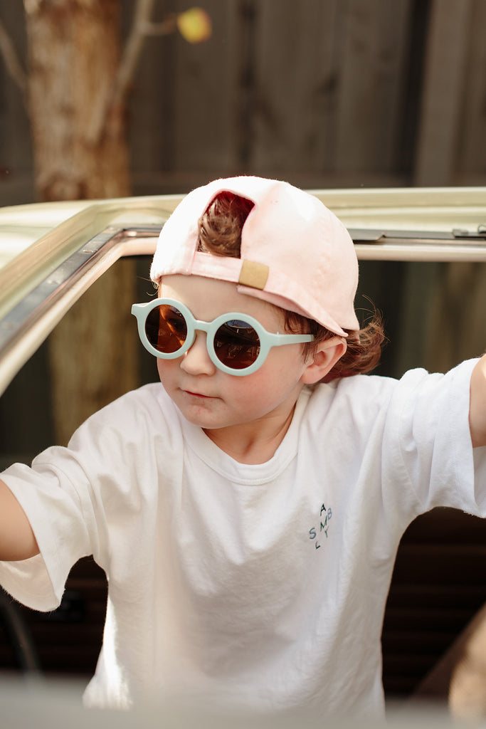 Sky-blue kids’ sunglasses with a rounded frame displayed on a soft cream background