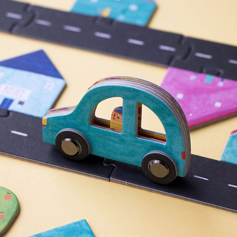 Close-up of a blue wooden toy car on the Londji Roads puzzle track surrounded by illustrated houses.