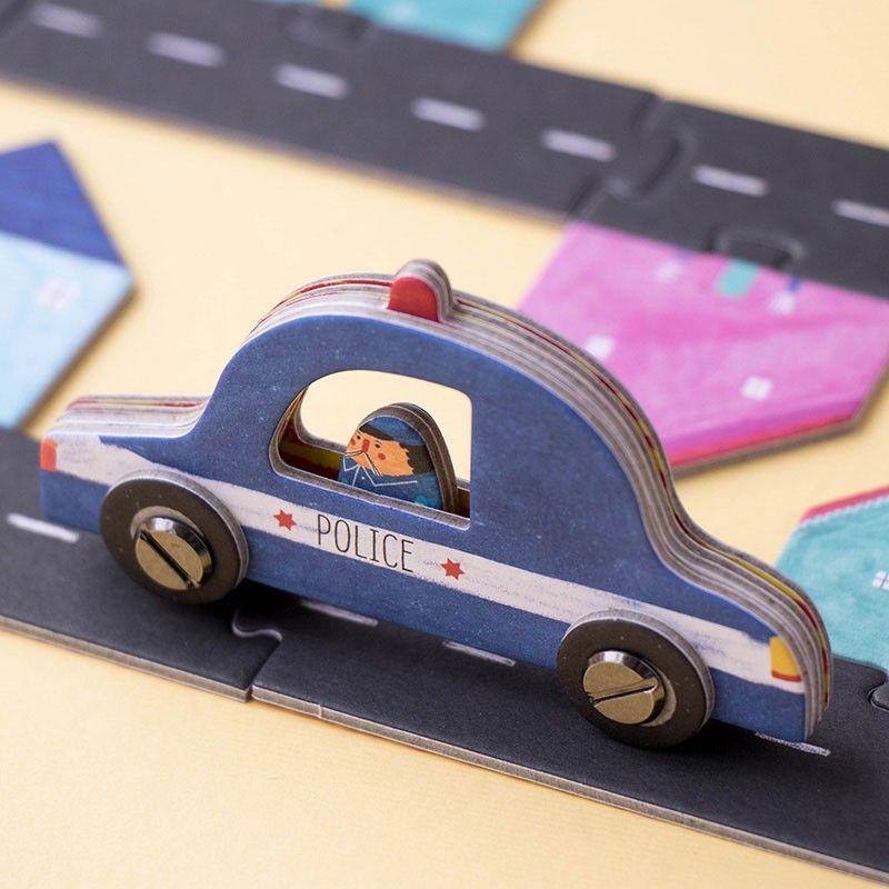Blue wooden police car from the Londji Roads game on a black road puzzle with colorful houses in the background.