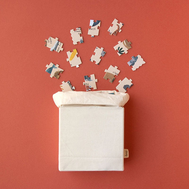 Londji Life Puzzle pieces spilling out of a white fabric bag onto a red surface.