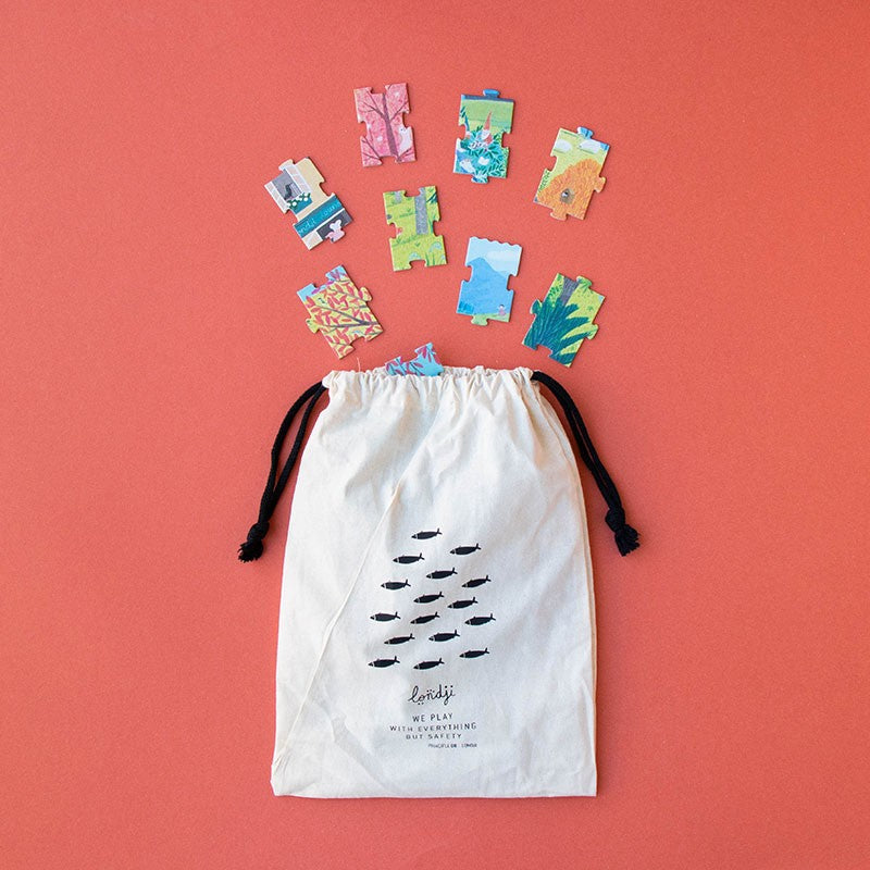 Puzzle pieces spilling from Londji fabric bag on red background.