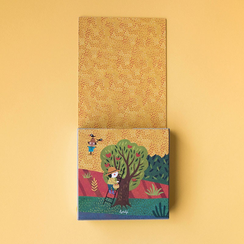 Partially opened box of Londji’s My Little Farm Pocket Puzzle with illustration of a farmer picking apples from a tree.