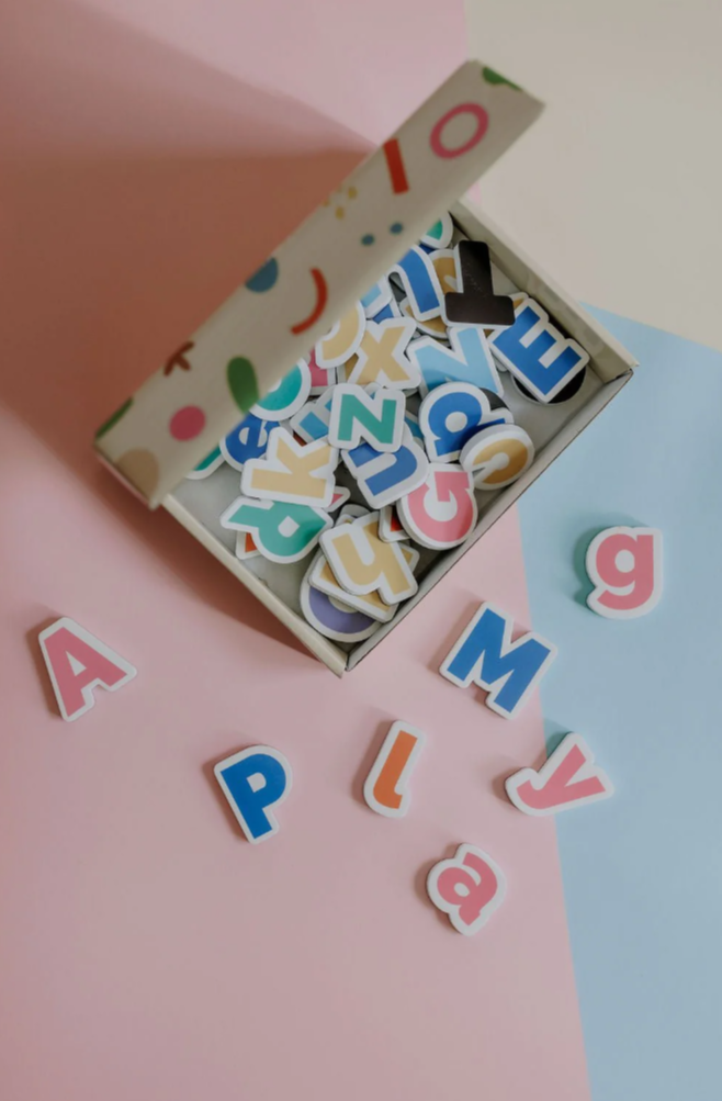 Open box of MagPlay alphabet magnets with bold, colourful letters, on a pastel backdrop.