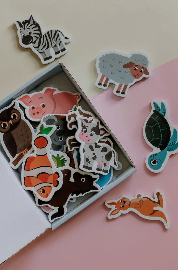 Top-down view of the open MagPlay Animal Magnet Kit featuring various animal magnets like a zebra, sheep, pig, and turtle on a pastel background.