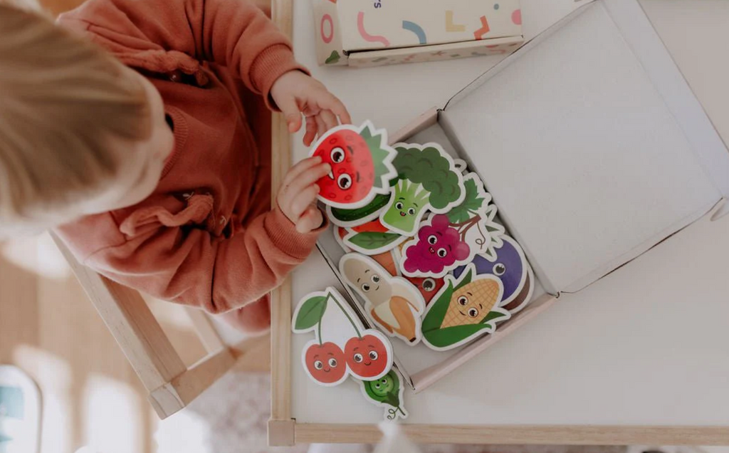 Overhead view of a child playing with the MagPlay Fruit & Vegetables Magnet Kit, sorting and exploring the bright fruit and veggie pieces.