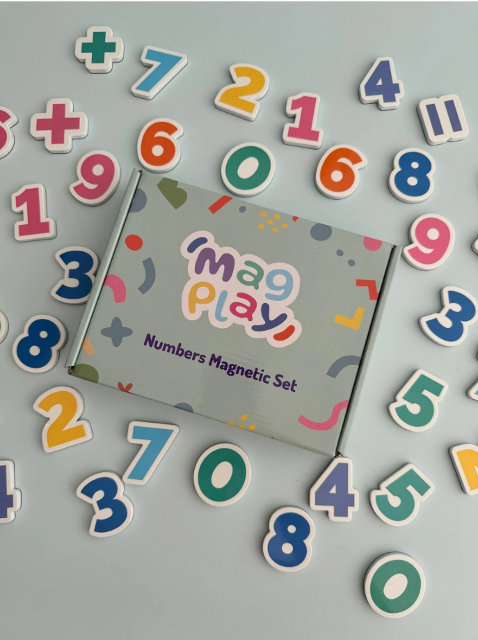 Tilted view of the MagPlay box with number magnets playfully scattered in a circular pattern on a grey surface.
