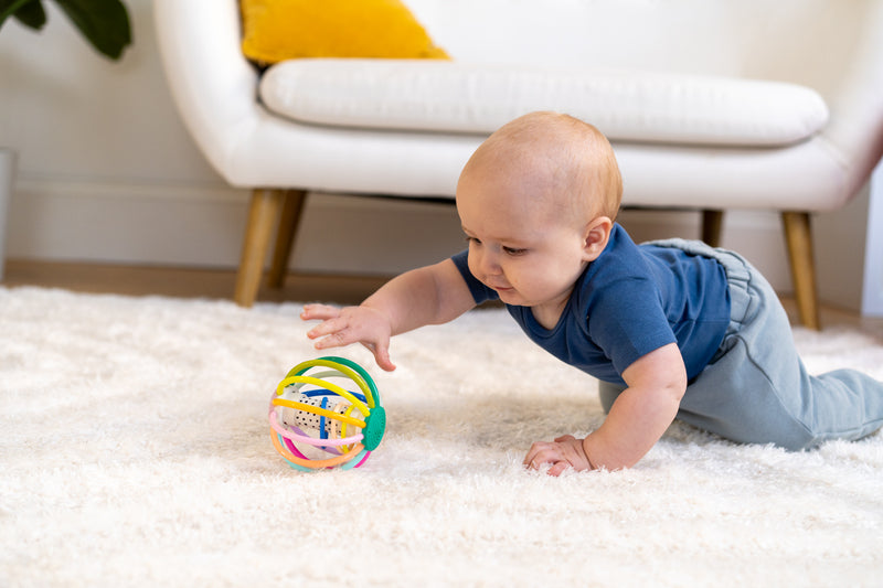 Infant playing with the Whistleball Colorpop on a nursery floor, rolling and grasping the toy, showcasing ideal playtime interaction for newborns and up.