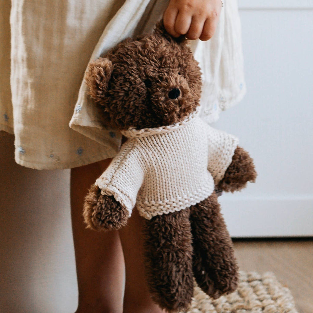Close-up of child’s hand holding Milo Bear plush toy, showing soft fabric and hand-knitted jumper.