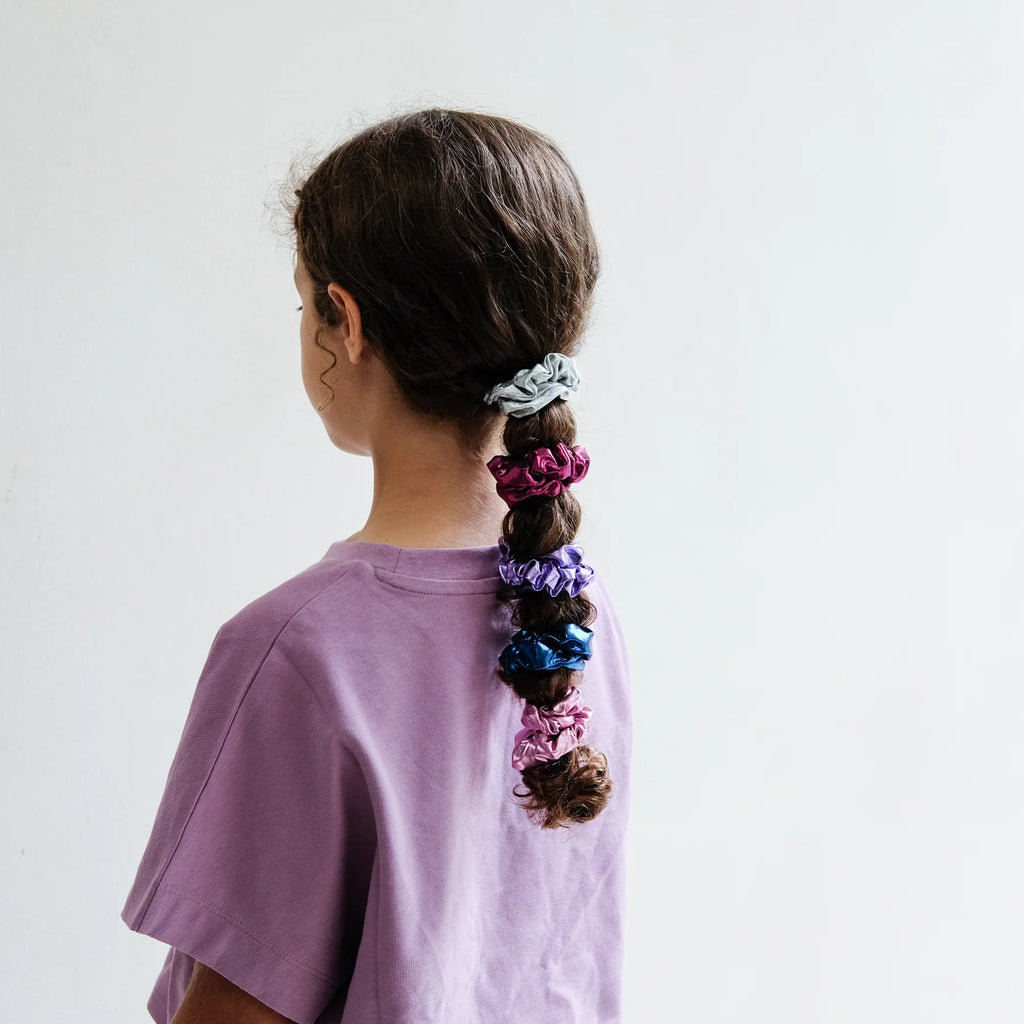 Girl wearing Mimi & Lula metallic scrunchies stacked down her braid in playful rainbow colors.
