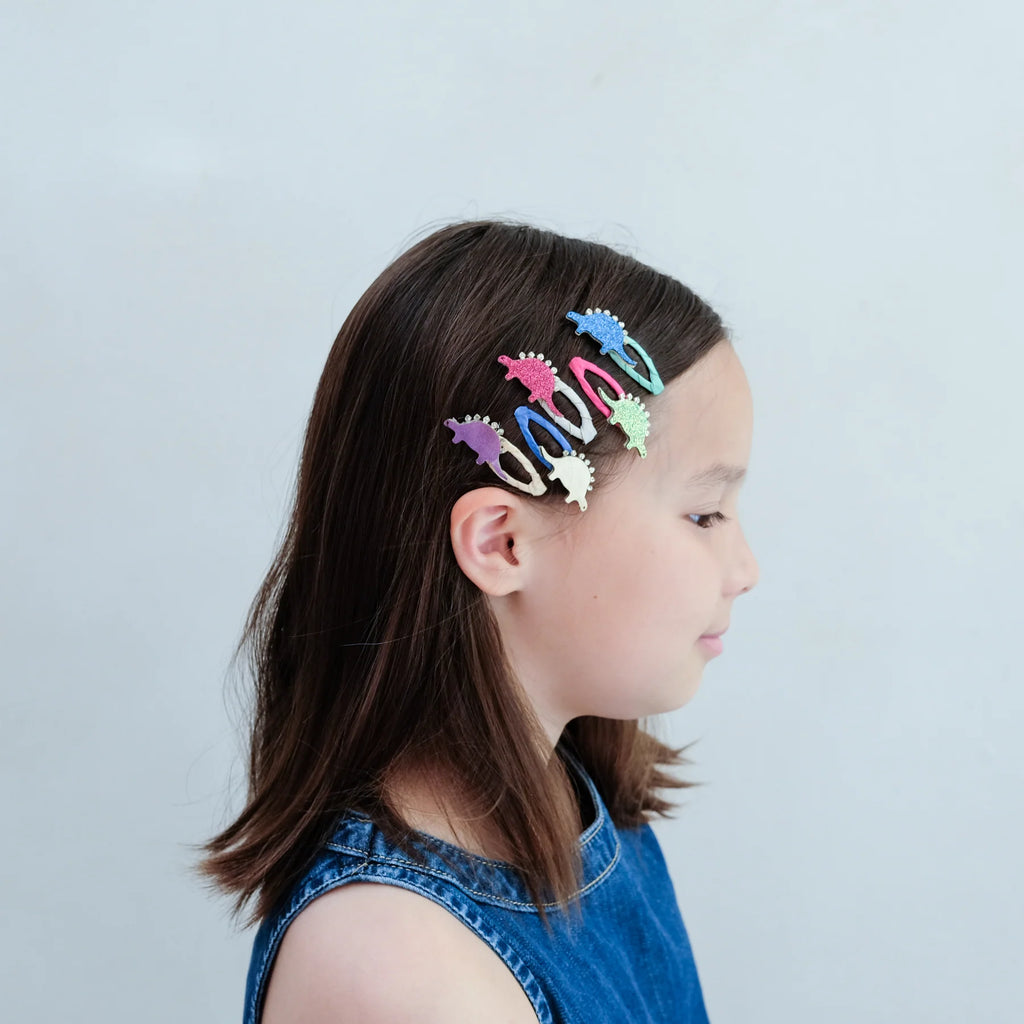 Little girl wearing colorful glitter dinosaur hair clips – fun stegosaurus kids hair accessories for playful hairstyles and dress-up looks.