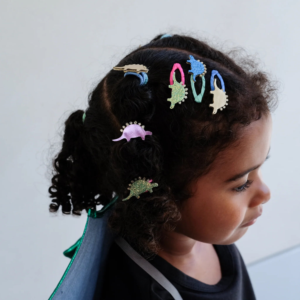 Smiling girl with curly hair wearing colorful glitter dinosaur hair clips – fun kids accessories for playful hairstyles and dress-up days.