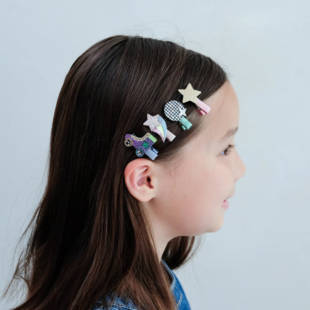 Young girl wearing Mimi & Lula Disco Diva Clips featuring glitter stars, disco balls, shooting stars, and roller skate designs.