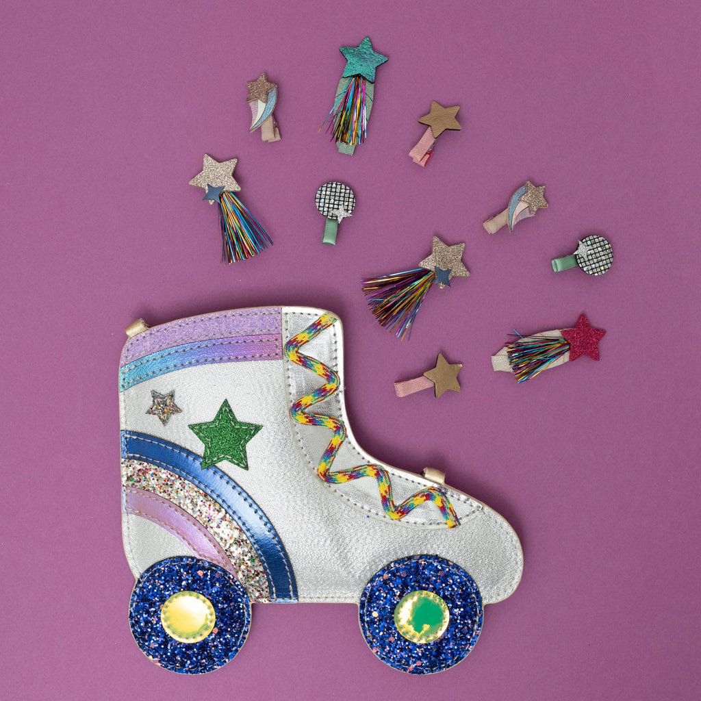 Flat lay of Mimi & Lula Disco Diva Clips and a glitter roller skate-shaped bag with stars and tassels on a pink background.