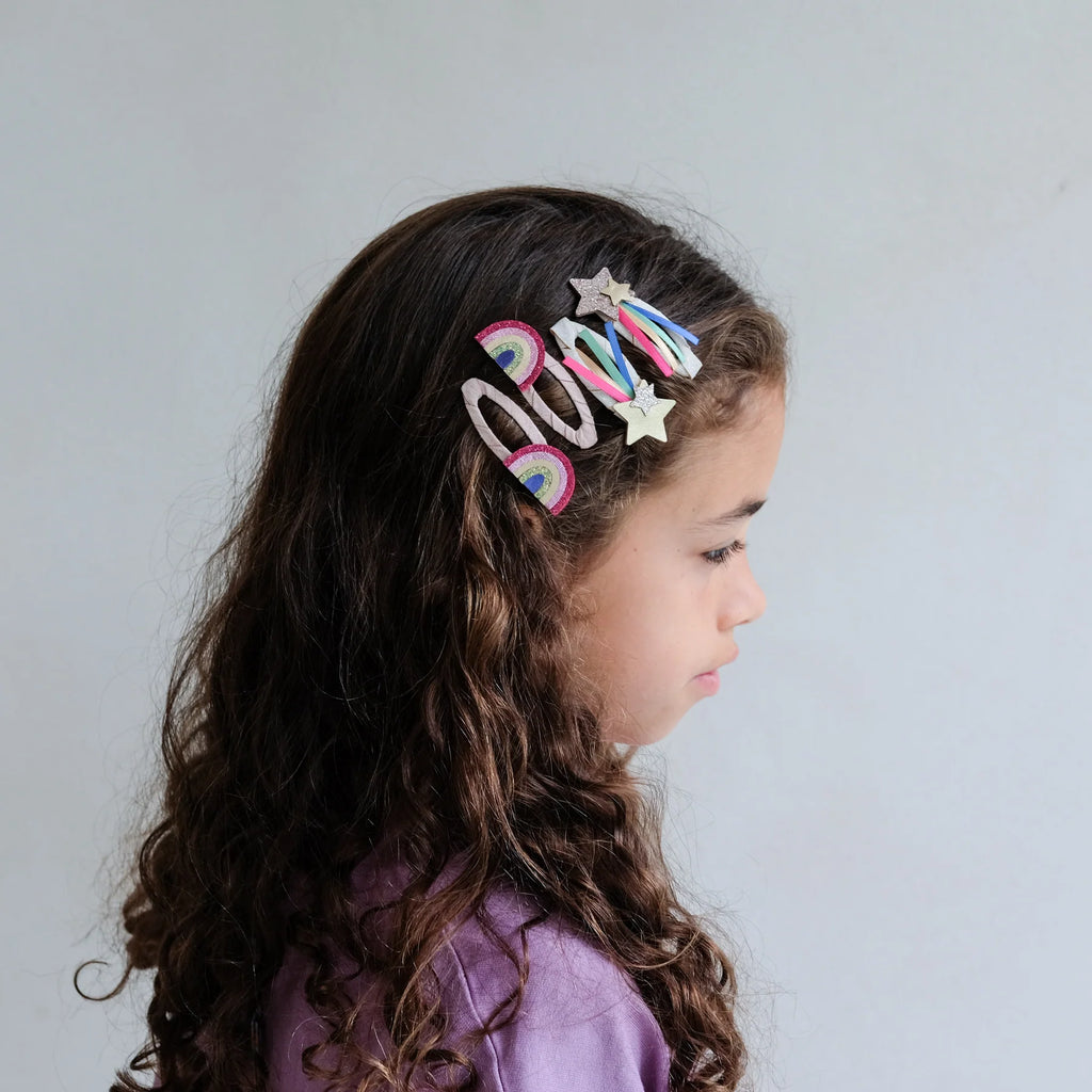 Young girl with curly hair wearing Mimi & Lula Disco O’Bow Clips shaped like rainbows and glitter stars.