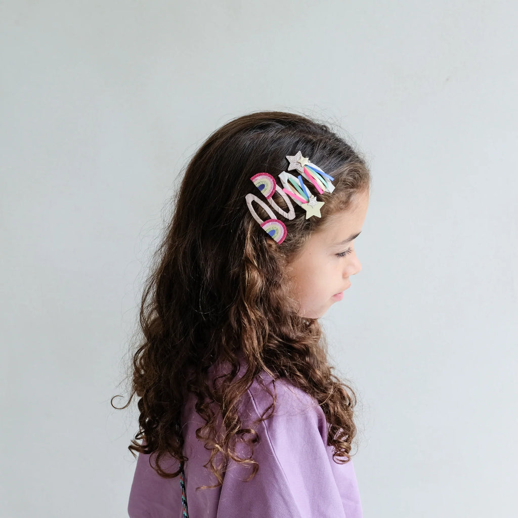 Girl wearing Mimi & Lula Disco O’Bow Clips featuring glitter stars and rainbow designs in her curly hair.