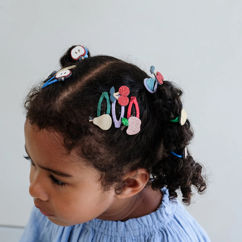 Child with curly hair wearing Mimi & Lula Fruity Mini Clic Clacs styled playfully.