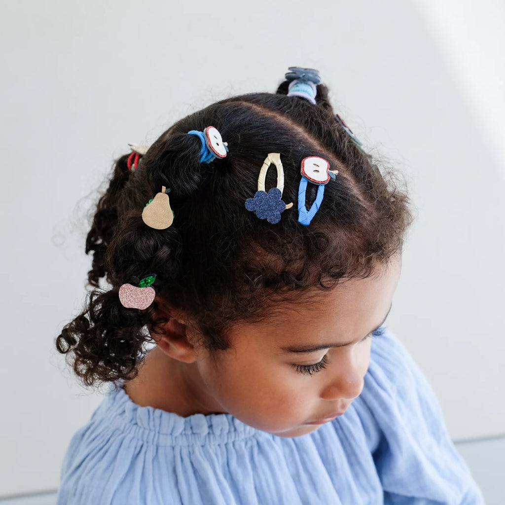 Close-up of child with curly hair wearing Mimi & Lula Fruity Mini Clic Clacs in blue and gold tones.