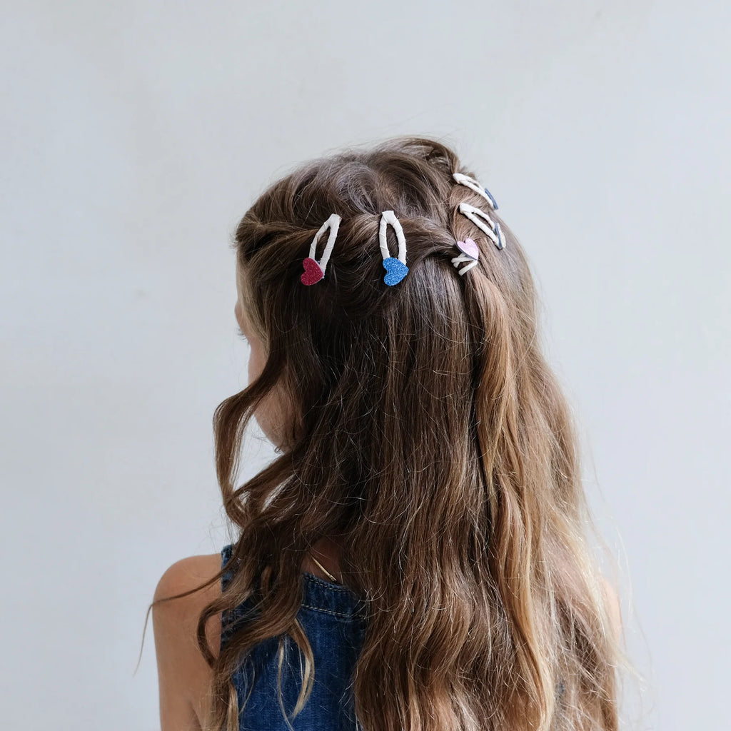 Girl wearing glitter heart hair clips in colorful shades, styled with wavy hair – cute and sparkly accessories for kids.
